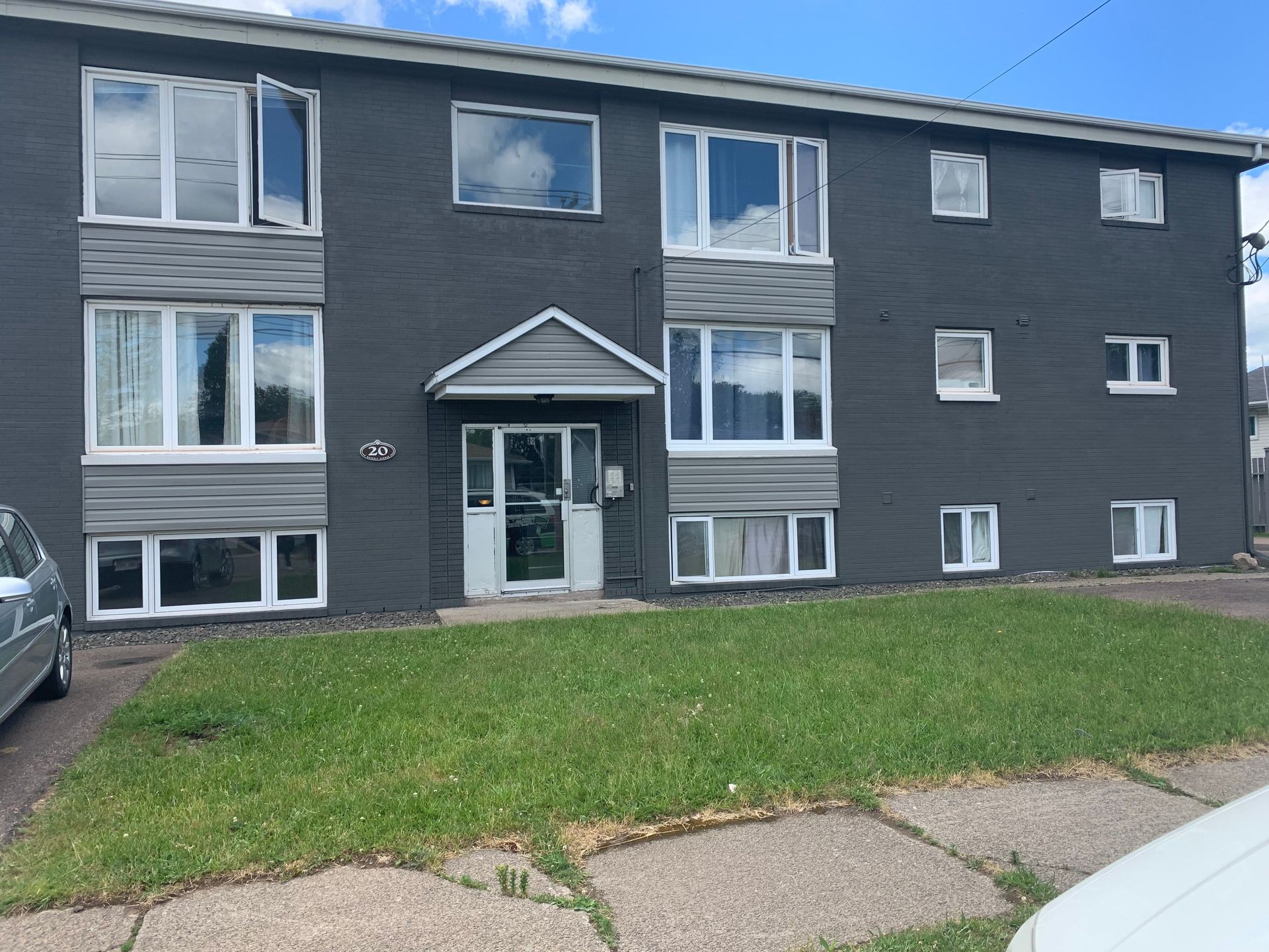 Exterior of a gray three-story apartment building with multiple windows and a green lawn in front.